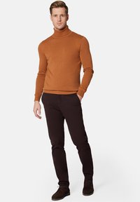Brązowy sweter w golf, z prążkowanymi mankietami i dołem, w połączeniu z ciemnymi spodniami i brązowymi butami. Prosty design, bez widocznych wzorów czy akcentów.