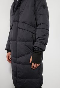 Le manteau matelassé noir présente un design matelassé avec une poche avant, des poignets ajustables et une coupe décontractée. Fabriqué à partir d'un matériau léger et résistant à l'eau.