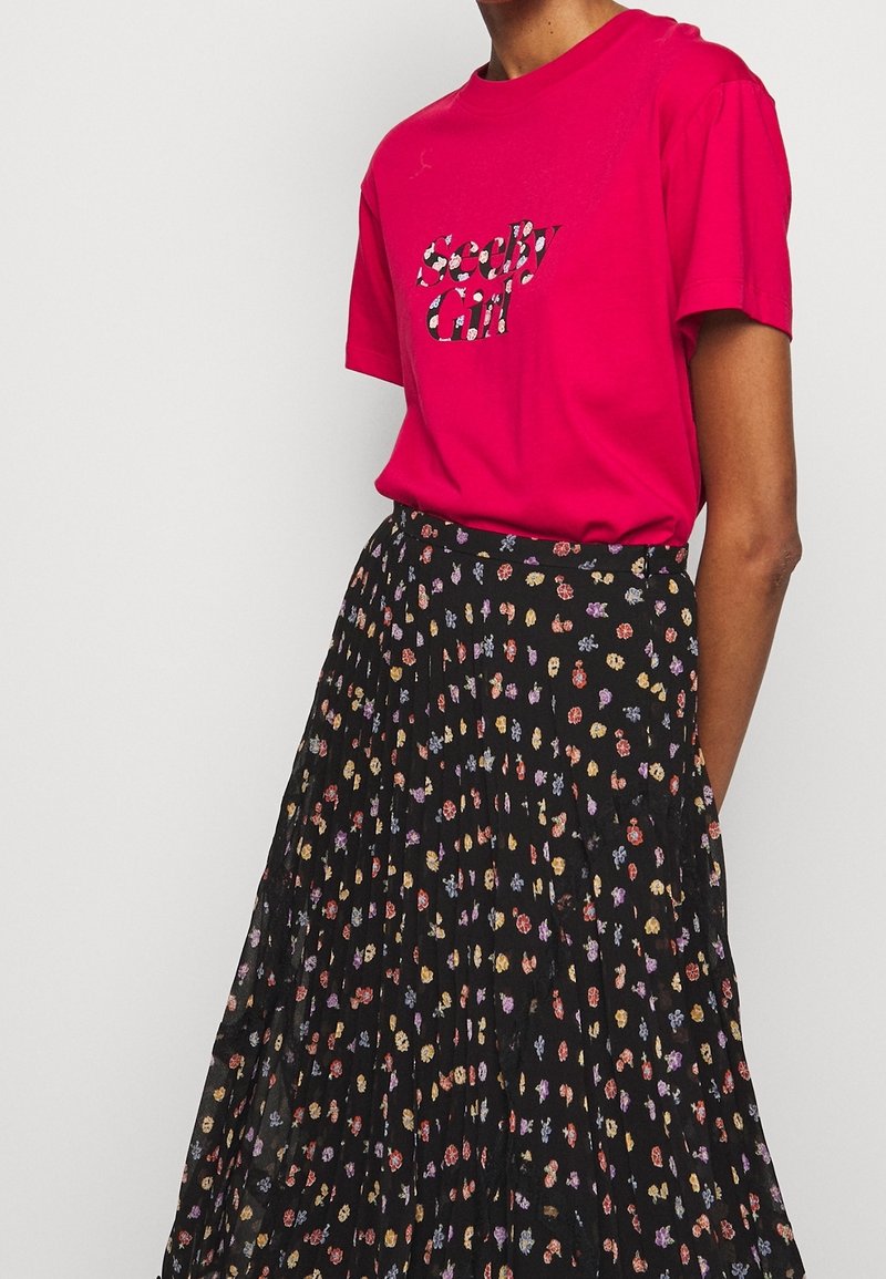 Fuchsia T-shirt med "Seedy Girl" grafik, parret med en sort plisseret nederdel med et multifarvet blomstermønster.