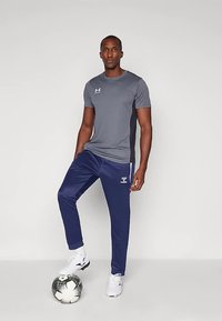 T-shirt desportivo cinza e calças de treino azul-marinho, ambos feitos de tecido leve. Detalhes discretos do logotipo e uma bola de futebol no chão.