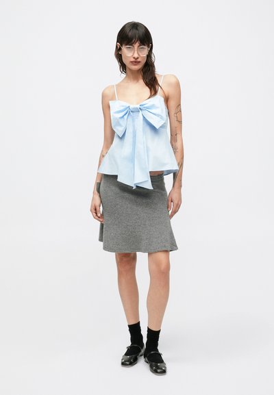 Svetlomodrý top bez rukávov s veľkou mašľou vpredu, skombinovaný so sivou sukňou po kolená. Má tenké ramienka a zvonový strih.