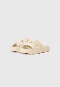 Light beige sandals with two wide straps and open toe. Made of smooth material, featuring a textured sole for grip.