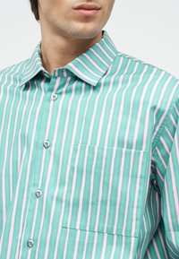 Man wearing a teal and pink vertically striped button-up shirt with a chest pocket and a classic collar, shown from the neck to mid-torso.