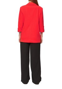 Blazer rouge à manches longues avec des poignets retroussés, fabriqué en tissu lisse. Associé à un pantalon large noir, créant une silhouette décontractée.