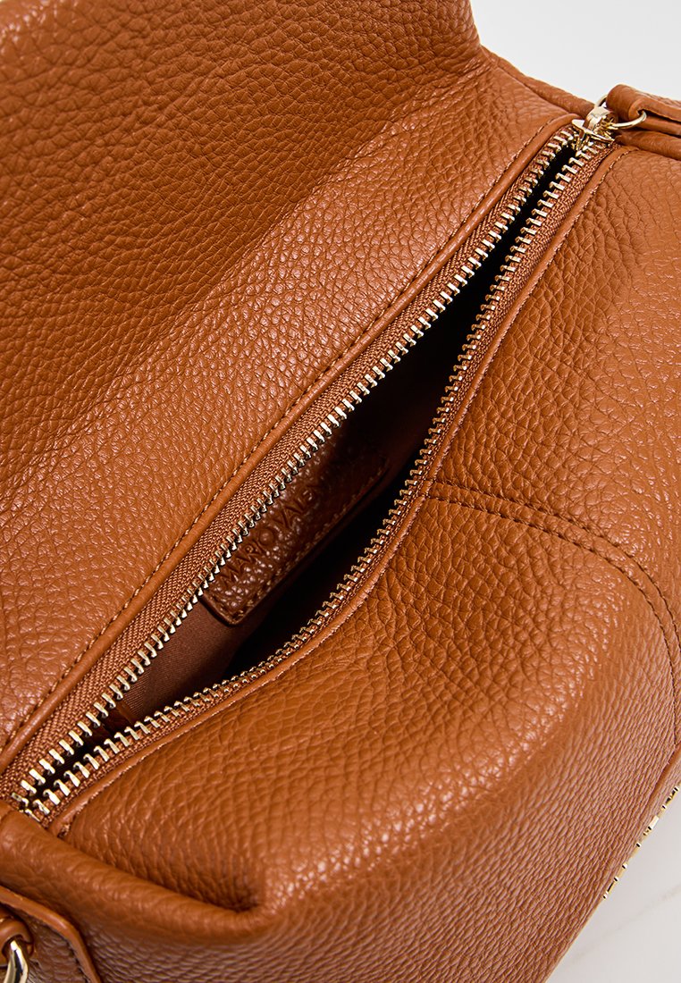 Sac en cuir brun texturé avec une fermeture éclair dorée partiellement ouverte révélant un intérieur brun et une étiquette en cuir à l'intérieur.