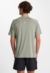 Maglietta atletica a maniche corte, di colore verde chiaro, con una texture liscia, dotata di maniche raglan e un piccolo logo sulla schiena.