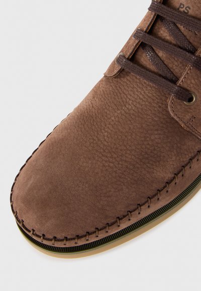 Scarpa in pelle marrone con una superficie texture, cuciture a contrasto e lacci rotondi. Presenta una suola piatta con un accento verde.