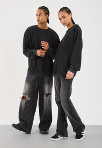 To modeller har på seg oversized svarte sweatshirt og grå ripte jeans. Antrekkene har en avslappet passform og varierte teksturer. Sneakers fullfører looken.