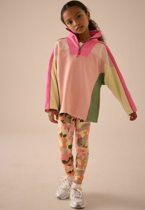 Kleurrijke oversized sweatshirt in roze, groen en crème. Bloemenpatroon legging in roze, oranje en groen. Witte sportschoenen.