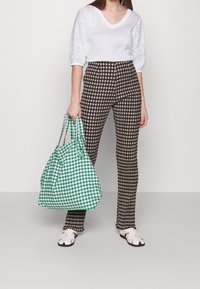 Bílý top s výstřihem ve tvaru V a krajkovými balónovými rukávy, hnědé kostkované kalhoty s vysokým pasem a zelená kostkovaná taška. Bílé sandály s uzavřenou špičkou.