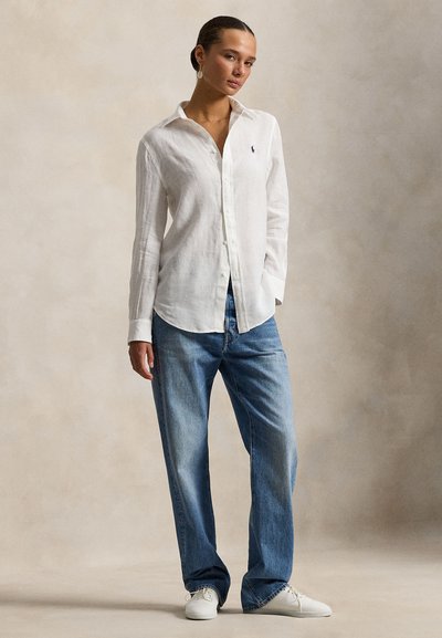 Λευκό πουκάμισο από λινό με κούμπωμα με κουμπιά, μακριά μανίκια· σετ με ανοιχτό μπλε τζιν παντελόνι φαρδιάς γραμμής και λευκά αθλητικά παπούτσια. Απλός σχεδιασμός, άνετη εφαρμογή.