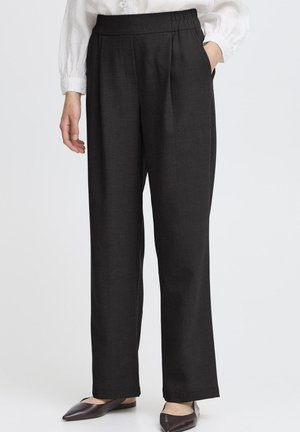 Black tailored trousers with a pleated front and elastic waistband. Smooth texture, straight-leg design. Worn with dark, pointed flats.