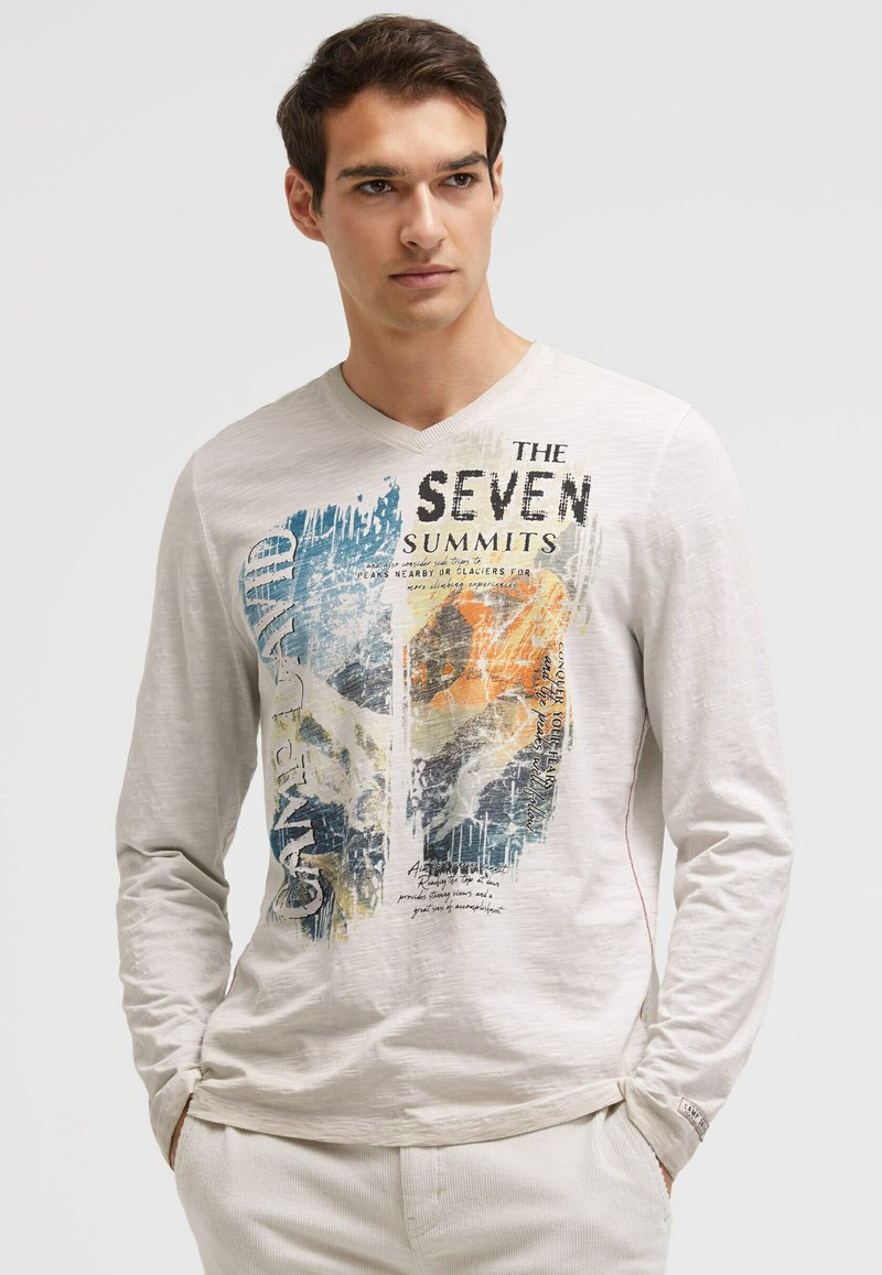 Langarm-T-Shirt in Hellgrau mit einem lebendigen Druck, der Text und abstrakte Formen in Blau, Orange und Grün auf einem strukturierten Stoff zeigt.