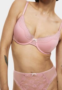Reggiseno rosa e slip in pizzo abbinati con un motivo testurizzato, caratterizzati da un delicato bordo in pizzo e un piccolo dettaglio a fiocco al centro davanti.