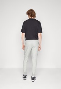 Svart T-shirt kombinerad med ljusgråa träningsbyxor. Outfiten har en avslappnad passform, mjuk textur och kontrasterande svarta och vita sneakers.