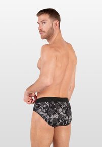 Schwarze Bikini-Briefs im Stil mit floralem und Schlangenleder-Design, elastischem Bund und passender Form, die einen strukturierten Stoff zur Schau stellen.
