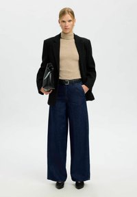 Platajiem tumša džinsu biksēm, beigu ribotam turtleneckam, melnam žaketam un struktūrētai melnai rokassomai. Gludie tekstūri un krāsu kontrasts.
