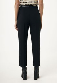 Svarta skräddarsydda byxor med rak passform, med en mjuk tyg, bältesöglor och en ren, elegant baksida som kompletteras av klackstövlar.