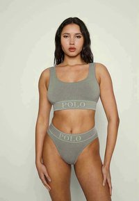 Bralette cinza com nervuras, alças largas e logotipo "POLO". Combinado com uma tanga de cintura alta correspondente, ambos exibindo uma textura suave.