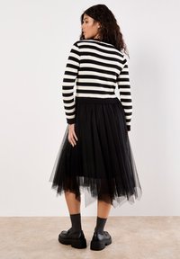 Maglione a righe bianco e nero abbinato a una gonna di tulle nera. L'outfit è completato da scarpe nere chunky e calze alla caviglia grigie.