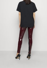 Černé oversized tričko, lesklé burgundské legíny, černé vysoké podpatky. Legíny mají lesklou texturu s kontrastním detailem po straně.