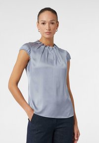 Himmelbluse mit kurzen Ärmeln aus Satin, mit gerafftem Ausschnitt und glatter Textur. Taillierte Passform mit abgerundetem Saum.