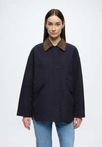 Tmavomodrá nepremokavá bunda s hnedým semišovým golierom, vybavená veľkými bočnými vreckami a voľným strihom. Hladká textúra a zapínanie na gombíky.