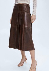 Bruine leren midi-rok met plooien, voorzien van een hoge taille en een gladde textuur. Gecombineerd met lichtgekleurde sandaaltjes met banden.