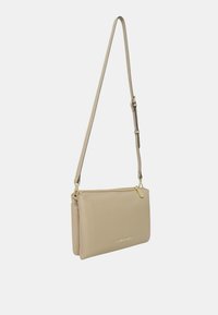 Borsa a tracolla in pelle beige con design piatto, dettagli in metallo dorato e tracolla regolabile; presenta una chiusura con zip e un marchio impressa.