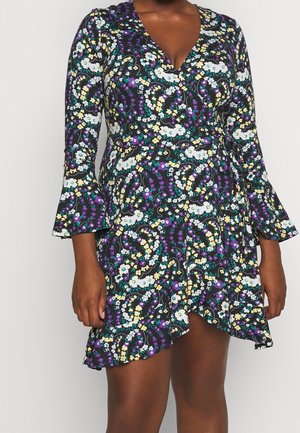 Nainen pukeutunut pitkähihainen, kukkakuvioinen kietaisumekko, jossa on violetteja, valkoisia, keltaisia ja teal-värisiä kukkia sekä röyhelöreuna.