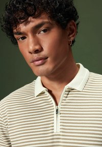 Gestreiftes Polo-Shirt mit Reißverschluss in Creme und Beige, aus strukturiertem Stoff und mit kontrastierendem Kragen; verfügt über ein silbernes Reißverschlussdetail.