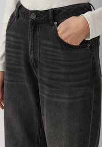 Pantaloni in denim neri con un design sbiadito, stile a cinque tasche e chiusura con bottone in metallo. Presenta una leggera texture sui pannelli frontali.