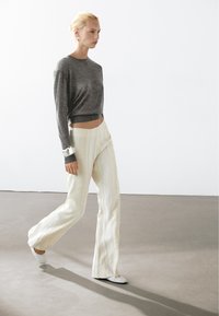 Grau geschnittener Pullover, cremefarbene weite Hose mit subtilen vertikalen Streifen und hellen Schuhen. Schlankes Design mit glatten Texturen.