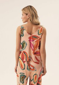 Top bez rękawów uszyty z miękkiego różowego materiału, zdobiony żywym, abstrakcyjnym wzorem liści w kolorach pomarańczowym, zielonym i magentowym, o luźnym kroju.