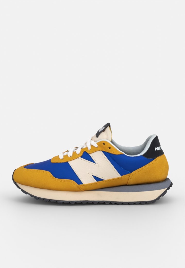 Blauwe en gele sneaker met een bovenwerk van suede en mesh, beschikt over een wit "N" logo, zwarte hielband en een gestructureerde rubberen zool.