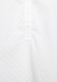 Camicia in tessuto bianco con un motivo testurizzato composto da piccoli punti in rilievo e una pattina di bottoni. Materiale in cotone leggero.