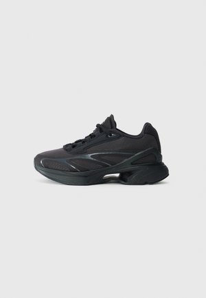 Schwarzer Sportschuh mit dicker Sohle, Mesh-Obermaterial und Schnürdesign, von der Außenseite auf einfarbigem Hintergrund gezeigt.
