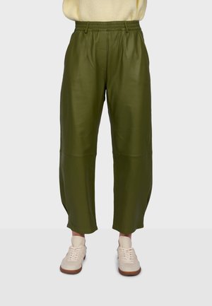 Pantalon large taille haute vert olive avec taille élastique, porté avec des baskets beige et un pull léger, sur un fond uni.