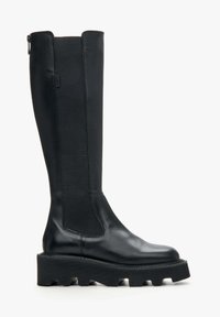 Black leather knee-high boot with textured side panels, chunky black rubber sole, and zipper detail at the back. Modern and sleek design.