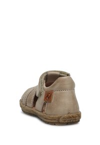 Beige lädersandal med utskärningsdesign, kardborreband, strukturerad sula och beige logotyp tygmärke. Rundad form och hållbar konstruktion.