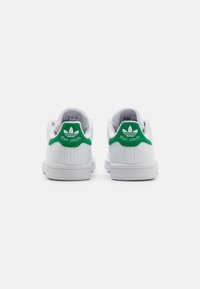 White sneakers with green accents, smooth leather material, flat sole, and a logo on the heel. Lace-free design, simple and classic silhouette.
