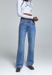 Jeans de tiro alto de color azul con un corte relajado, hechos de mezclilla. Cuenta con cinco bolsillos, un cierre de botón y un desvanecimiento sutil.
