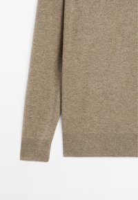 Beżowy sweter dziany o miękkiej teksturze, z okrągłym dekoltem i ściągaczami na mankietach oraz na dolnym brzegu. Gładki materiał o jednolitym wzorze.