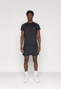 Μαύρο αθλητικό T-shirt με κοντά μανίκια, σε συνδυασμό με αντίστοιχες βερμούδες. Κατασκευασμένο από ελαφρύ ύφασμα. Ελάχιστη λεπτομέρεια λογότυπου στο στήθος.