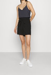 Svarta shorts med knytband i midjan, kombinerat med en marinblå linne och vita platåskor. Slätt tyg, avslappnad stil.