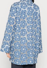 Chaqueta de patrón floral azul con un encaje superpuesto, con mangas largas y un corte relajado. El material parece ligero y transpirable.