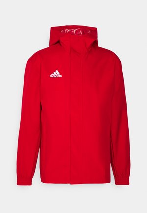Rote wasserdichte Jacke mit einem Frontreißverschluss, verstellbarem Kapuzenkragen und elastischen Bündchen. Mit weißem Adidas-Logo auf der linken Brust. Glatte Textur.