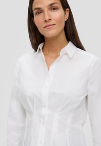 Camisa blanca de botones con un diseño estructurado, que presenta un cuello puntiagudo y costuras verticales, hecha de una tela suave y ligera.