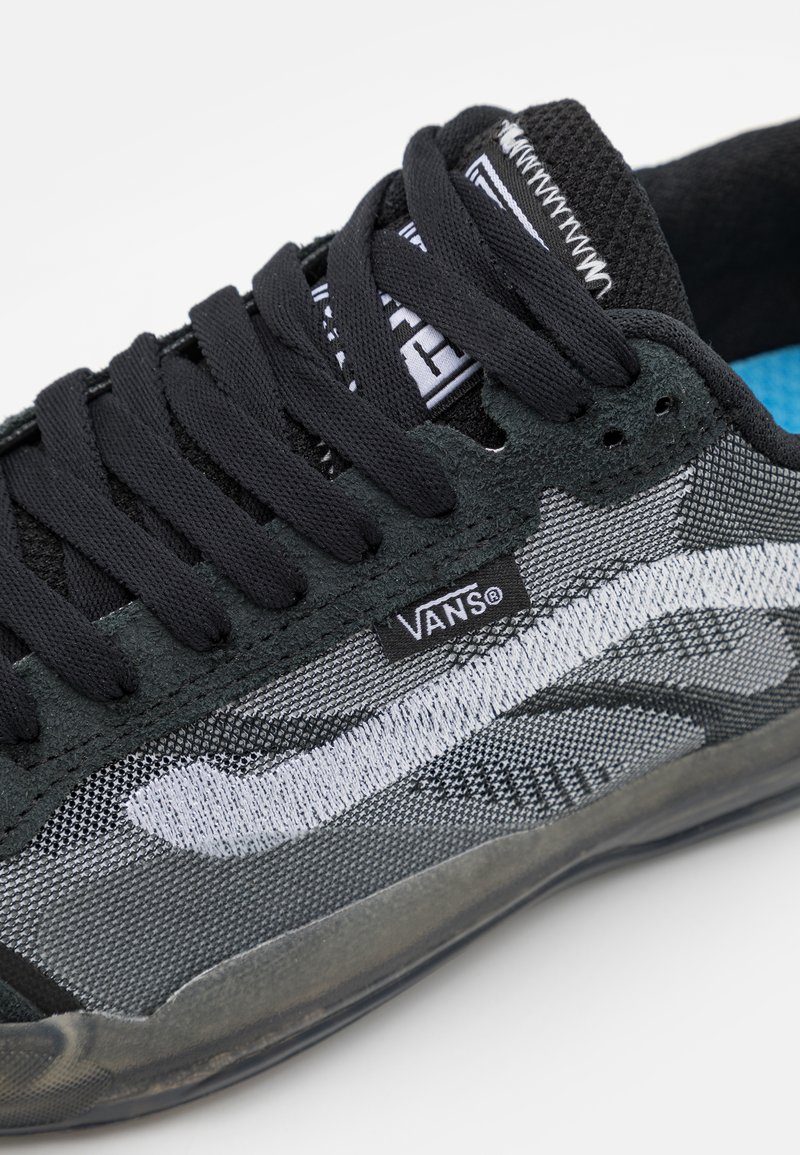 Zapatillas negras y grises con materiales de malla y ante, un logotipo de ola blanca y cordones negros. Notables detalles interiores en azul.