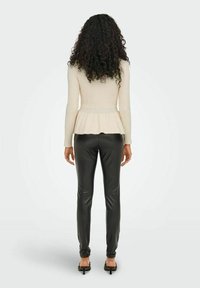 Cremefarbenes, geripptes Peplum-Oberteil mit langen Ärmeln, kombiniert mit enganliegenden schwarzen Hosen aus Kunstleder; mit ausgestelltem Saum in der Taille.